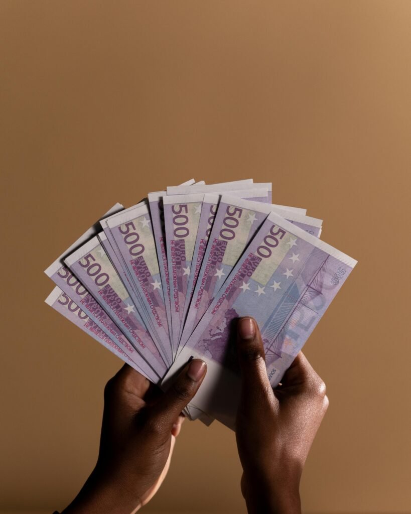 Close-up of hands holding multiple 500 euro banknotes against a beige backdrop.